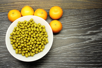green peas in a bowl and tangerines on a wooden surface