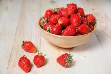 Fresh strawberries in a bowl on wooden table with low key scene.