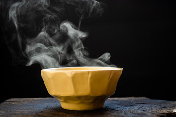 Steam of hot soup with smoke wood bowl on dark background.selective focus