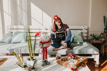 .Sweet and cheerful woman enjoying christmas at her home. Wearing christmas costume, having fun, eating sweets and having a letter blackboard of 