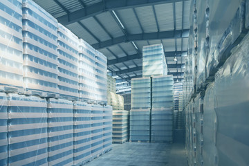 Obraz premium Interior of a modern warehouse in the blue toned Packing of bottles in the warehouse of the glass factory. Warehouse with packed glass bottles. Rows of shelves with goods.