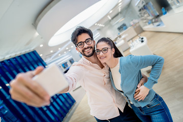 Cute couple taking self portrait and hugging while standing in tech store.  New technologies concept.