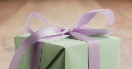 Closeup of green gift box with purple ribbon bow on old wood table