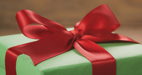 Closeup   of green paper gift box with red ribbon bow on oak table