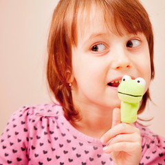 Finger puppet theatre. Cute little child girl playing with toys of green frog.