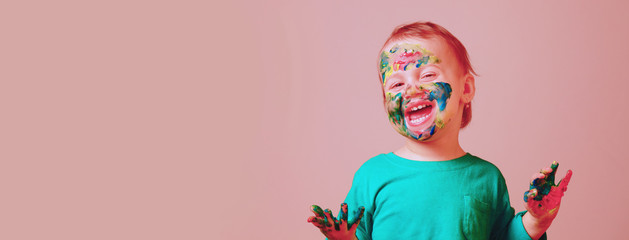 Humorous portrait of cute cheerful child girl laughing with painted in bright colors hands and face.