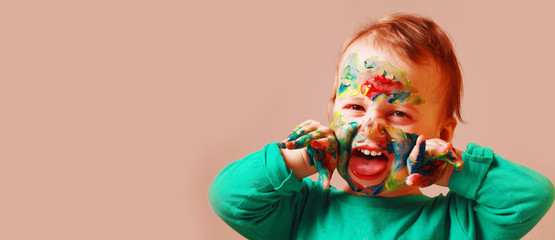 Funny face expression of cute cheerful child girl with colorful painting hands and face.