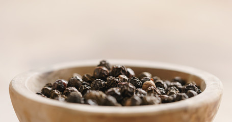 Fototapeta na wymiar Closeup of black dry pepper in wooden bowl on table