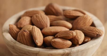Closeup   of organic almonds in wood bowl on wooden table