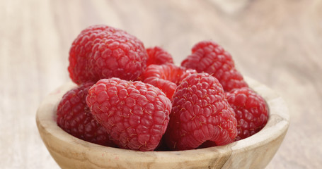 Closeup   of wood bowl full of ripe raspberries on old wooden table