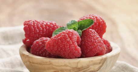 wood bowl full of ripe raspberries with mint leaves on old wooden table