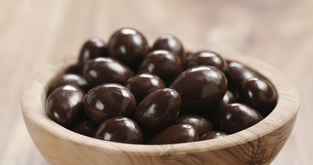 Closeup   of chocolate covered almonds in wood bowl on table