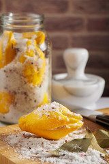 Cutted lemon in mix sea salt and spices, jar with salted lemons and mortar behind on brick wall background