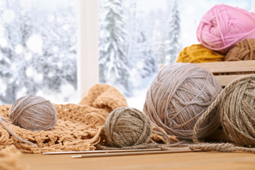 Obraz premium Woolen yarn and fabric on the window sill. Beautiful view outside the window - winter scenery and snow.