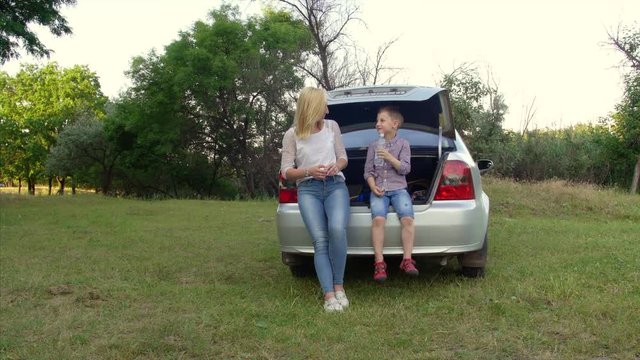4k Young woman and her son sit in the trunk of a car. Travel concept