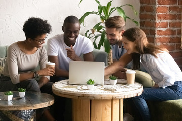 Happy smiling diverse friends using laptop together in cafe, watching funny video online, comedy movie during lunch in coffee house, multiracial people having fun together, free time activities