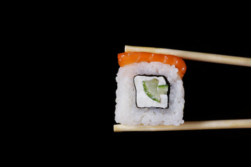 roll with salmon in chopsticks isolated. philadelphia roll isolated on black