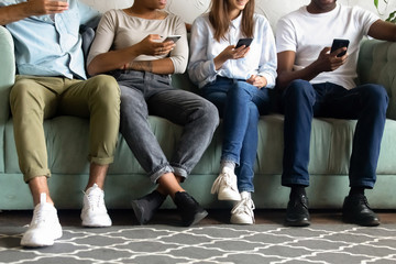 Close up diverse multiracial people, friends sit on couch, sofa together, using electronic mobile...