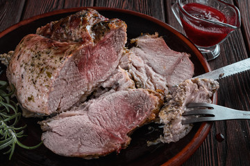Hot baked ham on a dark ceramic plate next to a sprig of rosemary, cranberry sauce on a wooden background