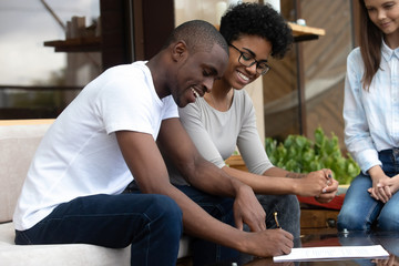Happy African American couple signing contract, making agreement with businesswoman, female realtor, wedding planner, financial advisor, smiling clients with seller in cafe, successful negotiations