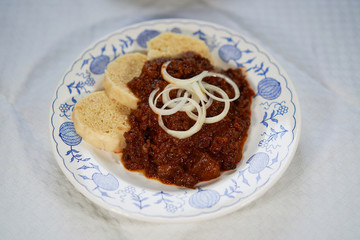 Close up picture of slow cooked czech or hungarian beef goulash stew served with traditional czech dumplings and choped fresh onion on the rustic plate. 