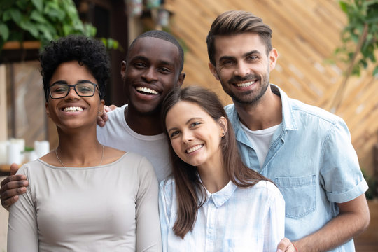 Head shot portrait of happy multiethnic friends look at camera, smiling diverse people having fun together in cafe, excited African Ameirican and caucasian colleagues, students posing, making photo