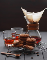 Coffee brewing gadget. Coffee in a chemex jar and glasses served with oatmeal cookies on dark background