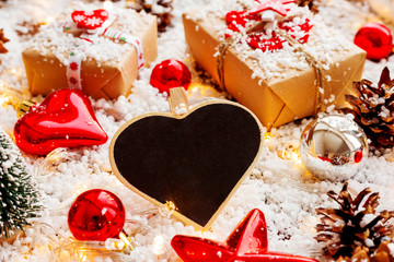 Christmas and New year background with presents, ribbons, balls and different decorations on snow.Clear heart chalkboard for your text.