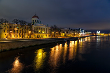 Fototapeta premium Neva river embankment with historical buildings on the shore and reflection of night lights in the water, beautiful sunset sky. Petersburg, Russia