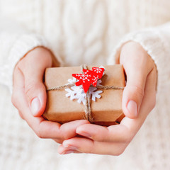 Woman in knitted sweater is holding Christmas present packed in craft paper with felt snowflake and red fir tree. New Year DIY gift.