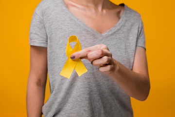 Young female holding yellow gold ribbon awareness symbol for endometriosis, suicide prevention,...