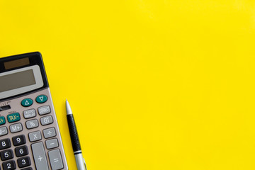 Flat lay or top view of pen with calculator on vivid yellow background table with blank copy space, math, cost, tax or investment calculation