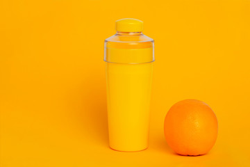 Yellow bottle on a yellow background next to an orange. Minimalism