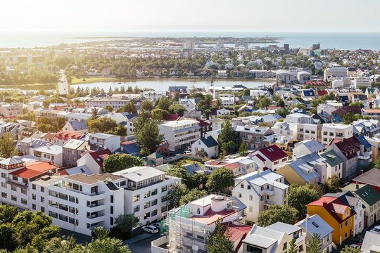 Panoramic view from above on cozy city neighborhood with green trees, pond and sea harbour in clear sunny summer day. Reykjavik, Iceland