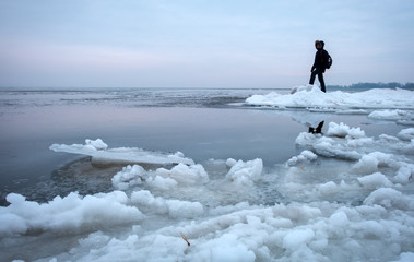 Man with backpack on the coast of frozen river during sunset. Traveler concept