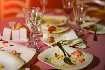 Dirty empty dishes with wasted food on served festive table after dinner party. Leftovers, empty plates after banquet.
