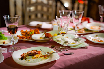 Plates with crumbs of food and glasses for wine on the table with pink tablecloth in the restaurant. Remains of food in plates after lunch or dinner.