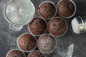 Fresh muffins with sugar icing on a wooden black table.