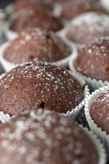 Fresh muffins with sugar icing on a wooden black table.