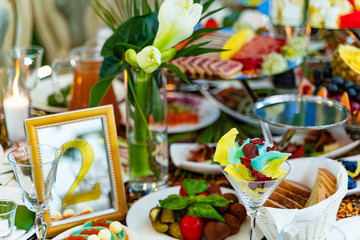 Festively served table with different food, decorated with flowers for banquet, restaurant interior. Plenty of tasty food for guests.