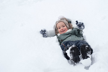 Fototapeta na wymiar Little boy lying on his back in the snow and having fun while snow is falling