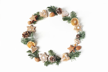 Fototapeta na wymiar Christmas circle floral composition. Wreath of fir tree branches, pine cones, gingerbread cookies and dry orange slices on white background. Winter holiday design. Flat lay, top view.