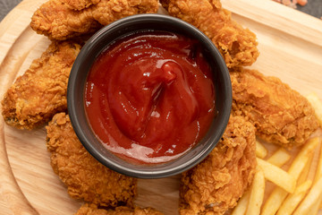 Chicken strips and tomatoes ketchup on a wooden tray.