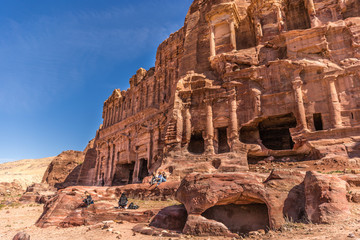 Petra, Jordan - Feb 26th 2018 - A group of tourist sitting in front of a giant temple full of details in Petra in a blue sky day