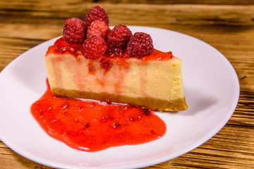 White plate with cheesecake New York and raspberries on wooden table