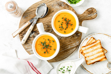 pumpkin or carrot or sweet potato vegetable soup in white bowls served on a light background, top view