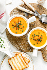 pumpkin or carrot or sweet potato vegetable soup in white bowls served on a light background, top view