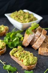Fresh bread with Mexican homemade guacamole on a black table.