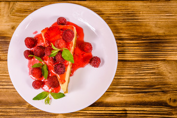 White plate with cheesecake New York, leaves of mint and raspberries on wooden table. Top view
