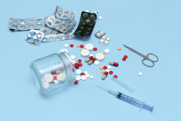 Fototapeta na wymiar A scattering of pills, capsules,empty blisters, syringe and scissors on a blue background
